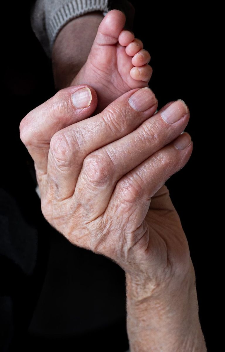 Intergénérationnel — main âgée tenant le pied du nouveau-né