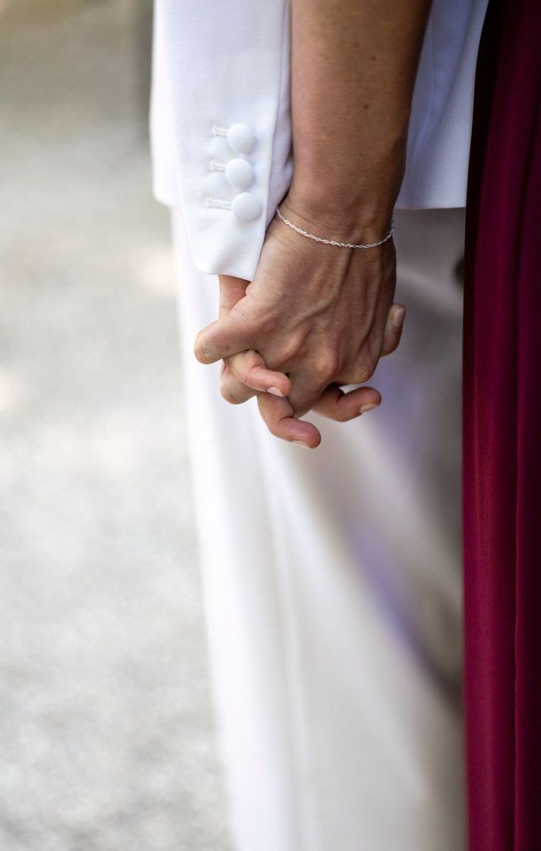 Mariage — mains enlacées des mariées, bracelet et costume bordeaux